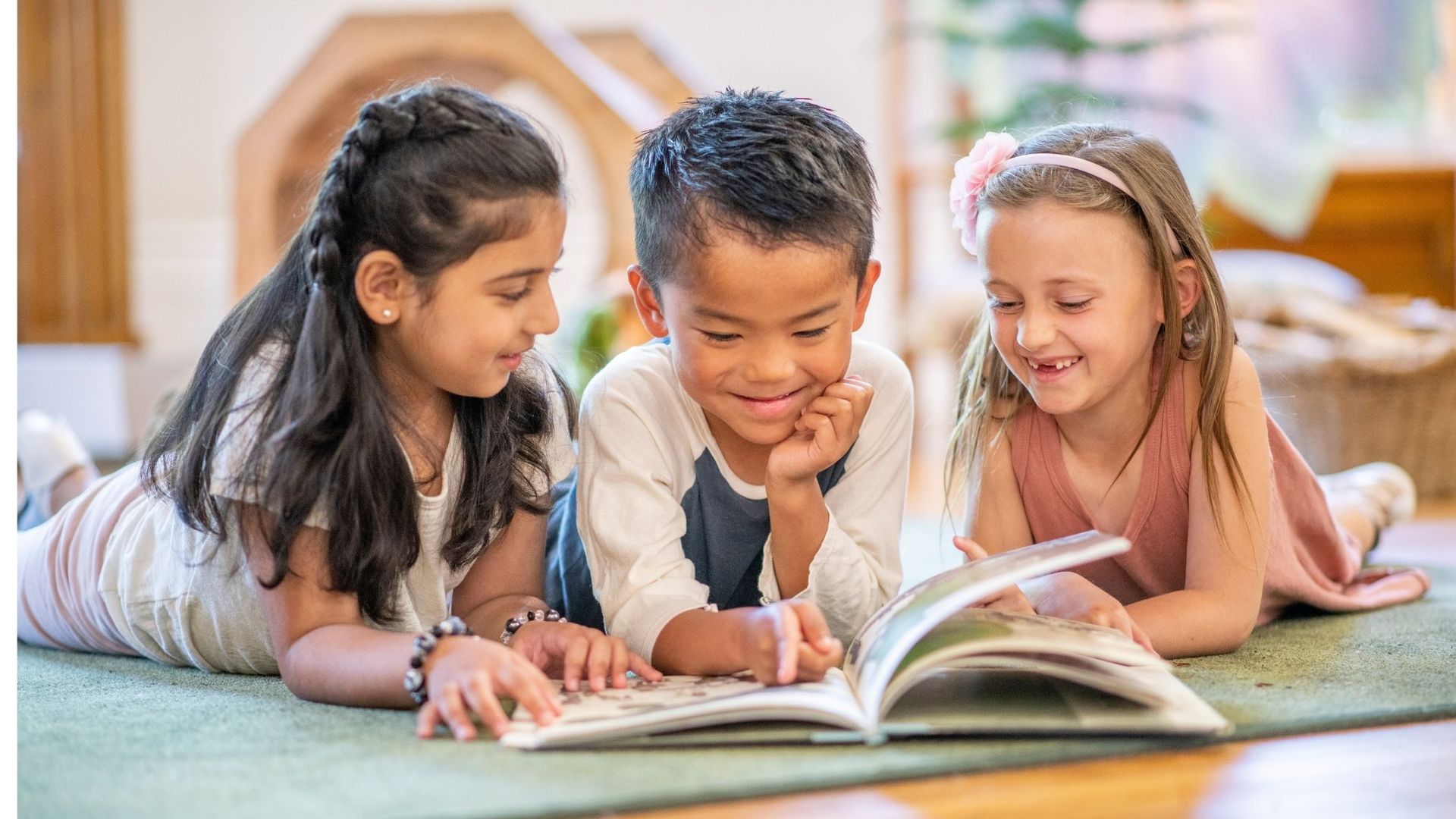Three children reading a book together on a rug, smiling.