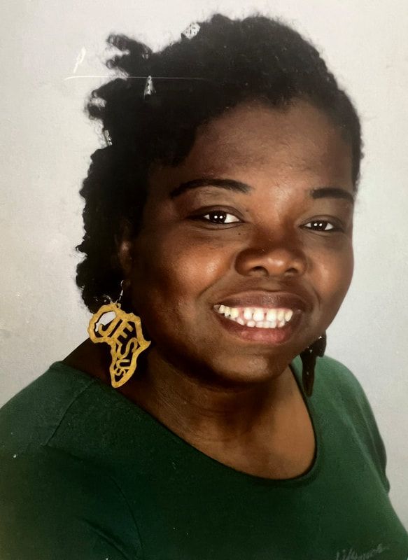 A woman wearing a green shirt and earrings is smiling