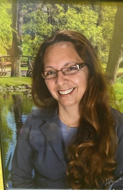 A woman wearing glasses and a blue jacket is smiling for a picture.