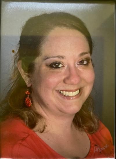 A woman in a red shirt and red earrings is smiling for the camera.