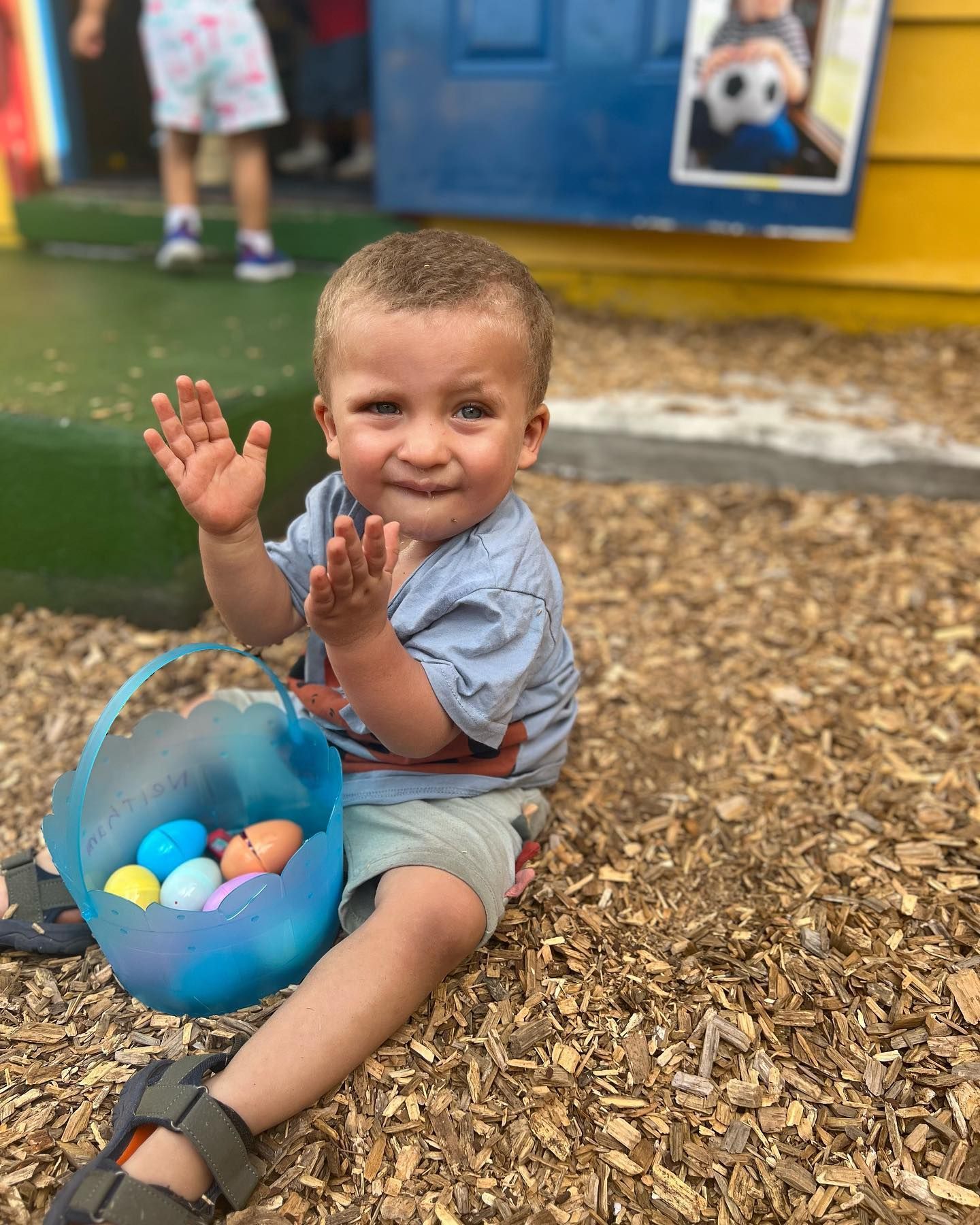 A little boy is sitting on the ground with a basket of easter eggs.