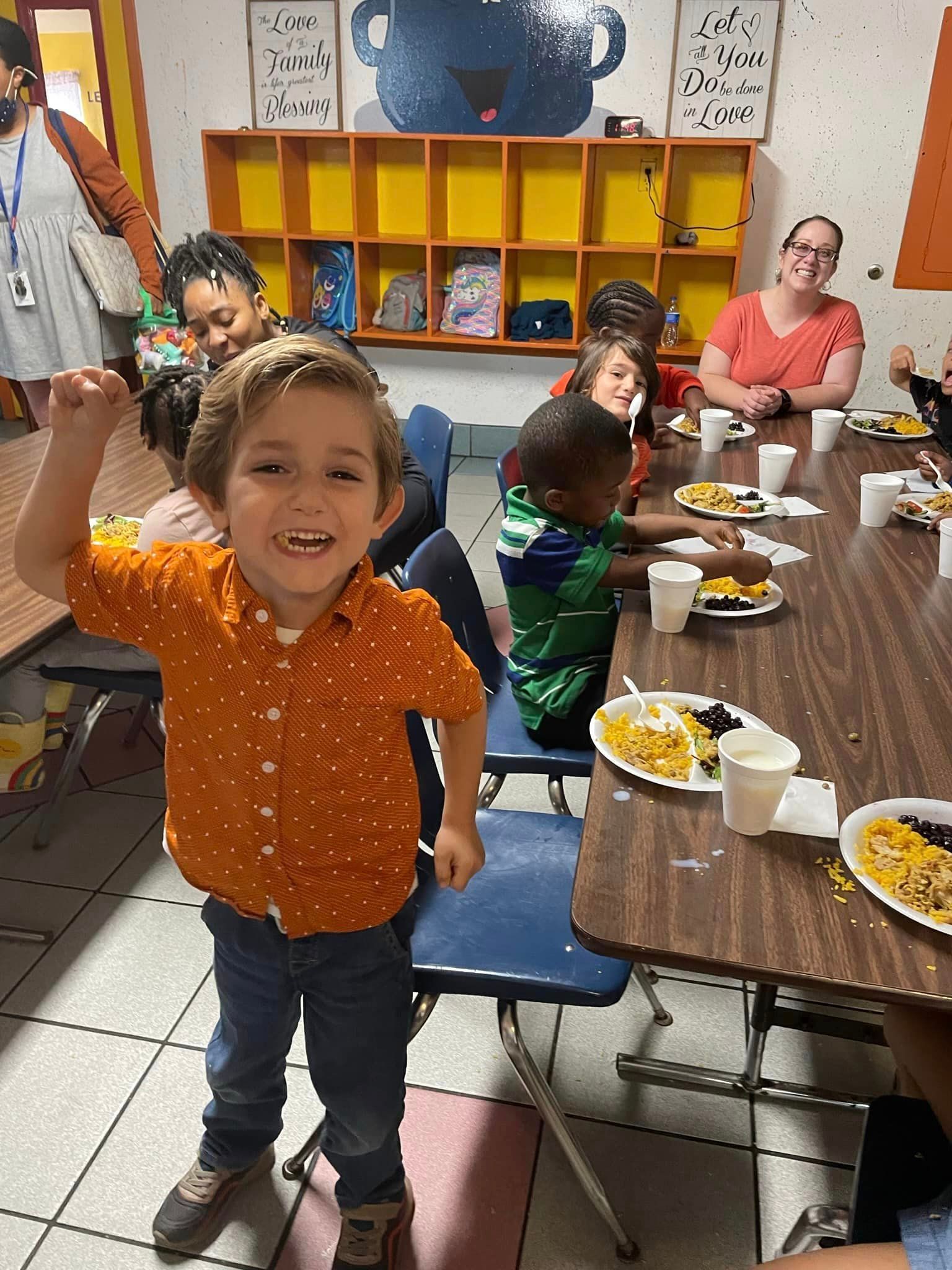 A group of children are sitting at tables with plates of food.