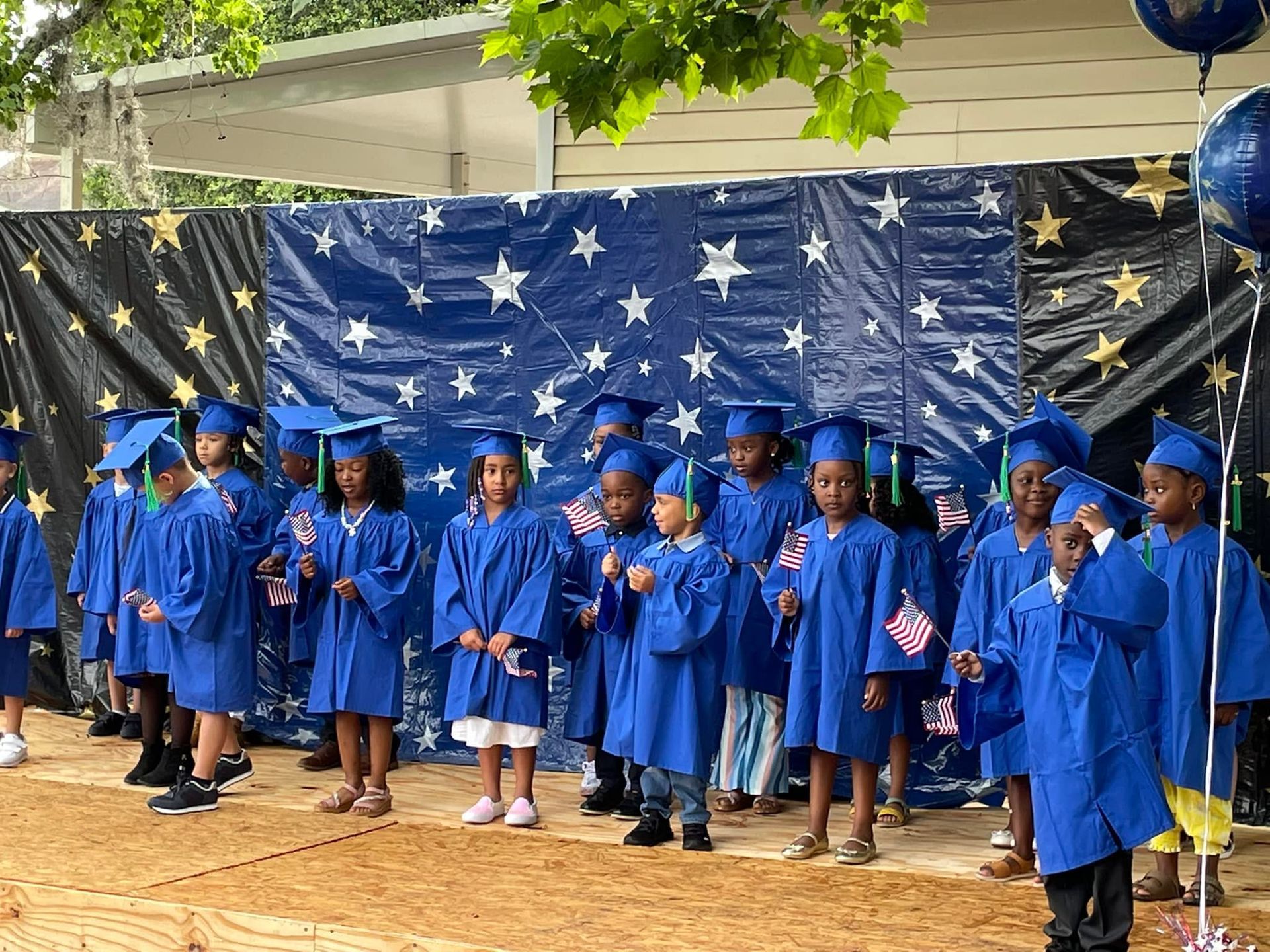 A group of children in graduation caps and gowns are standing on a stage.
