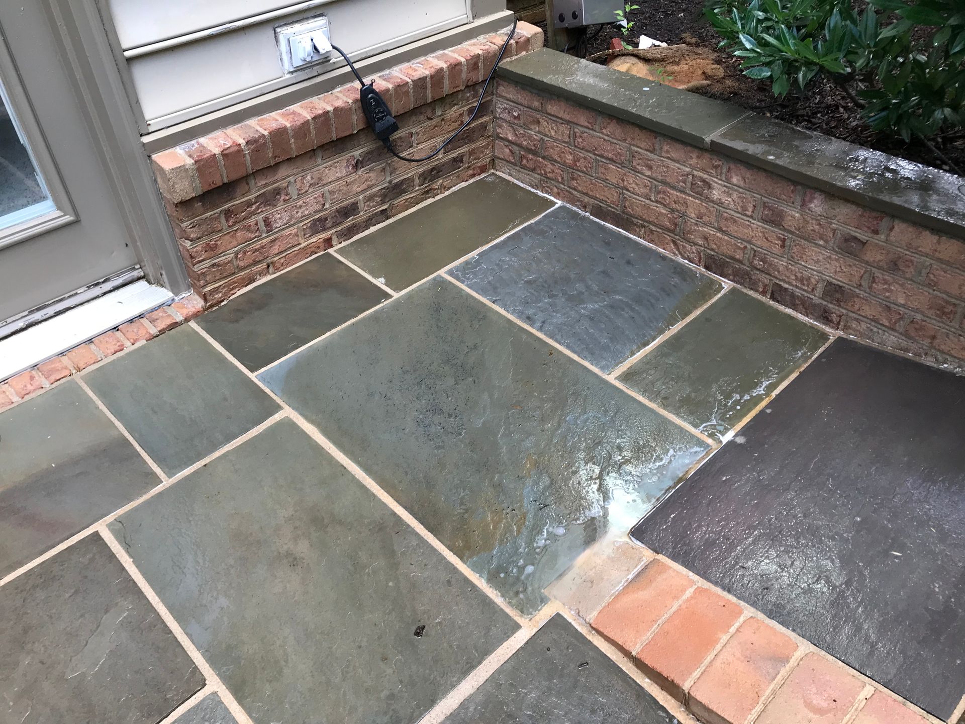 Patio paved with rectangular grey stones, bordered by brick and a building exterior.
