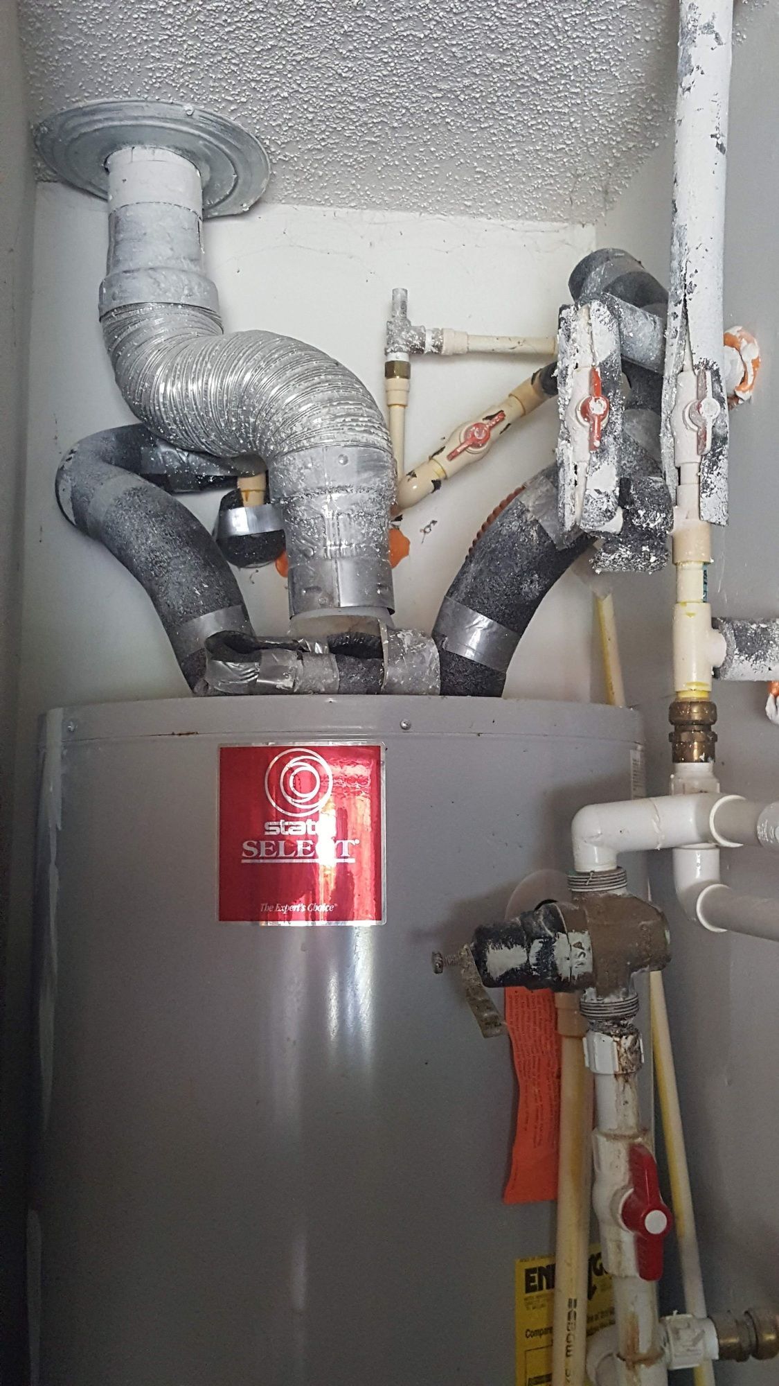 A water heater is sitting in a room next to pipes.