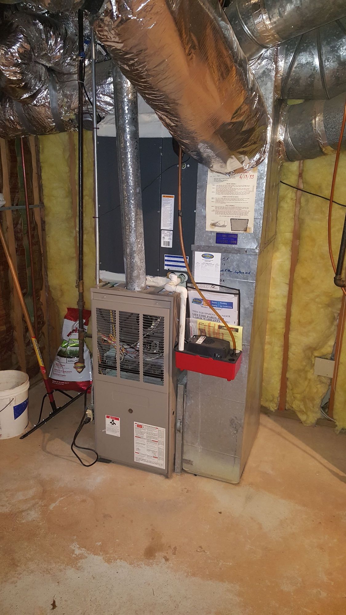 A furnace is sitting in a basement next to a broom.