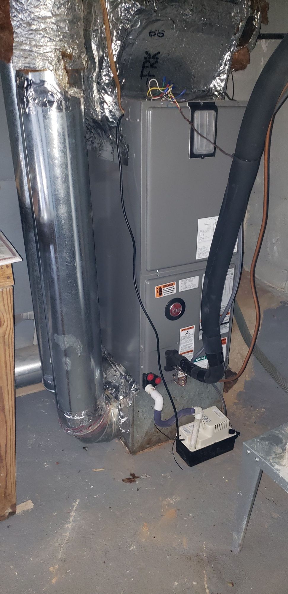A furnace is sitting in a basement next to a vacuum cleaner.