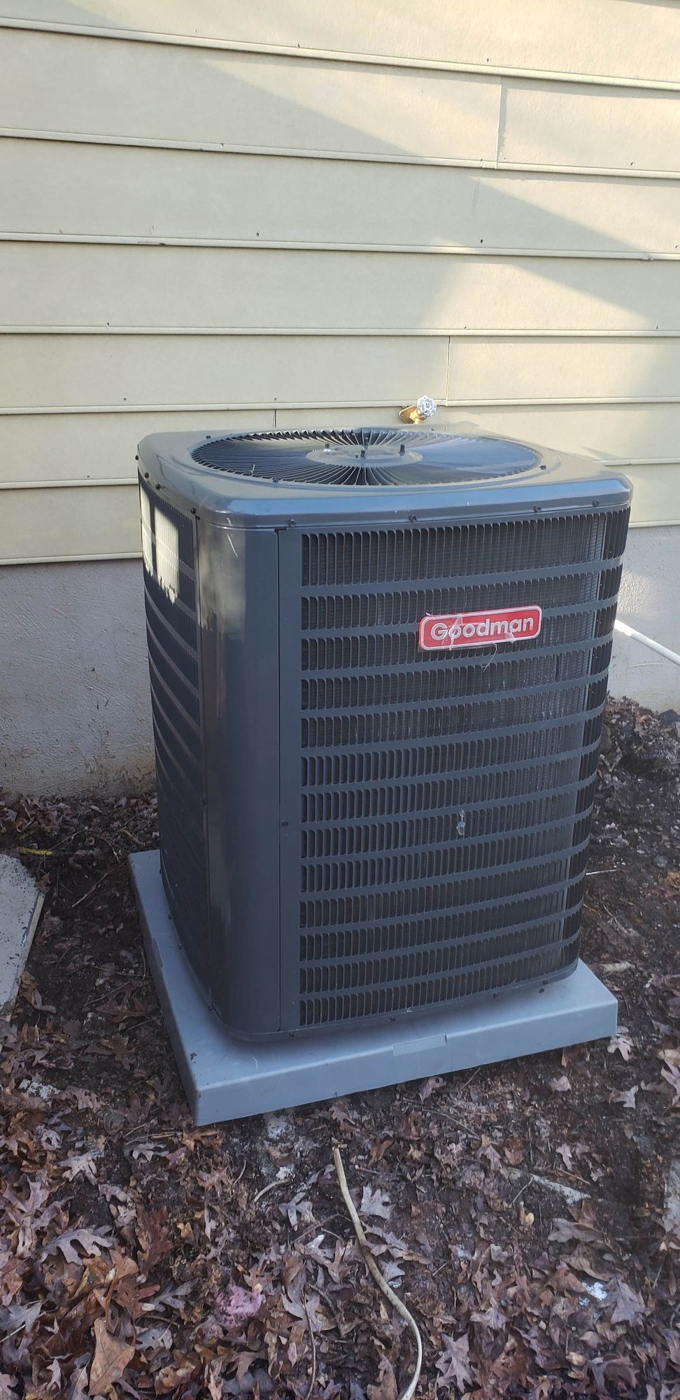 A black air conditioner is sitting on the ground in front of a house.