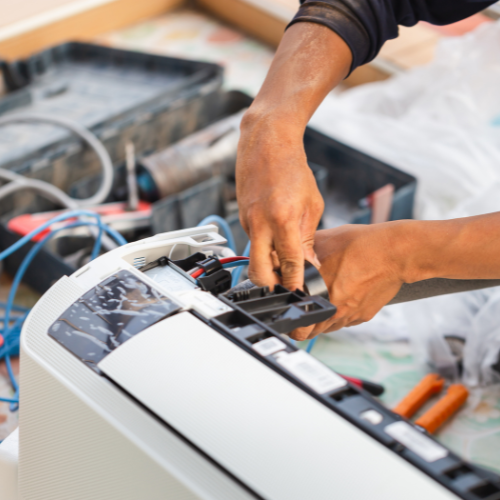 A man is fixing an air conditioner with a pair of pliers