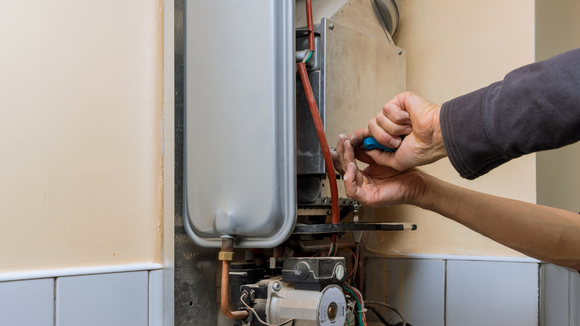 Person using a screwdriver to repair a furnace; indoor setting with beige walls.