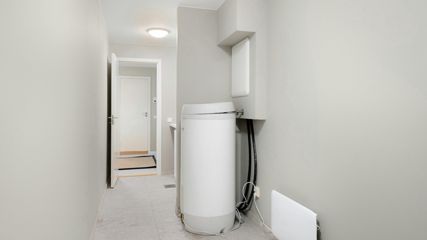 Narrow utility room with a tall white water heater, grey walls, and a door at the end.