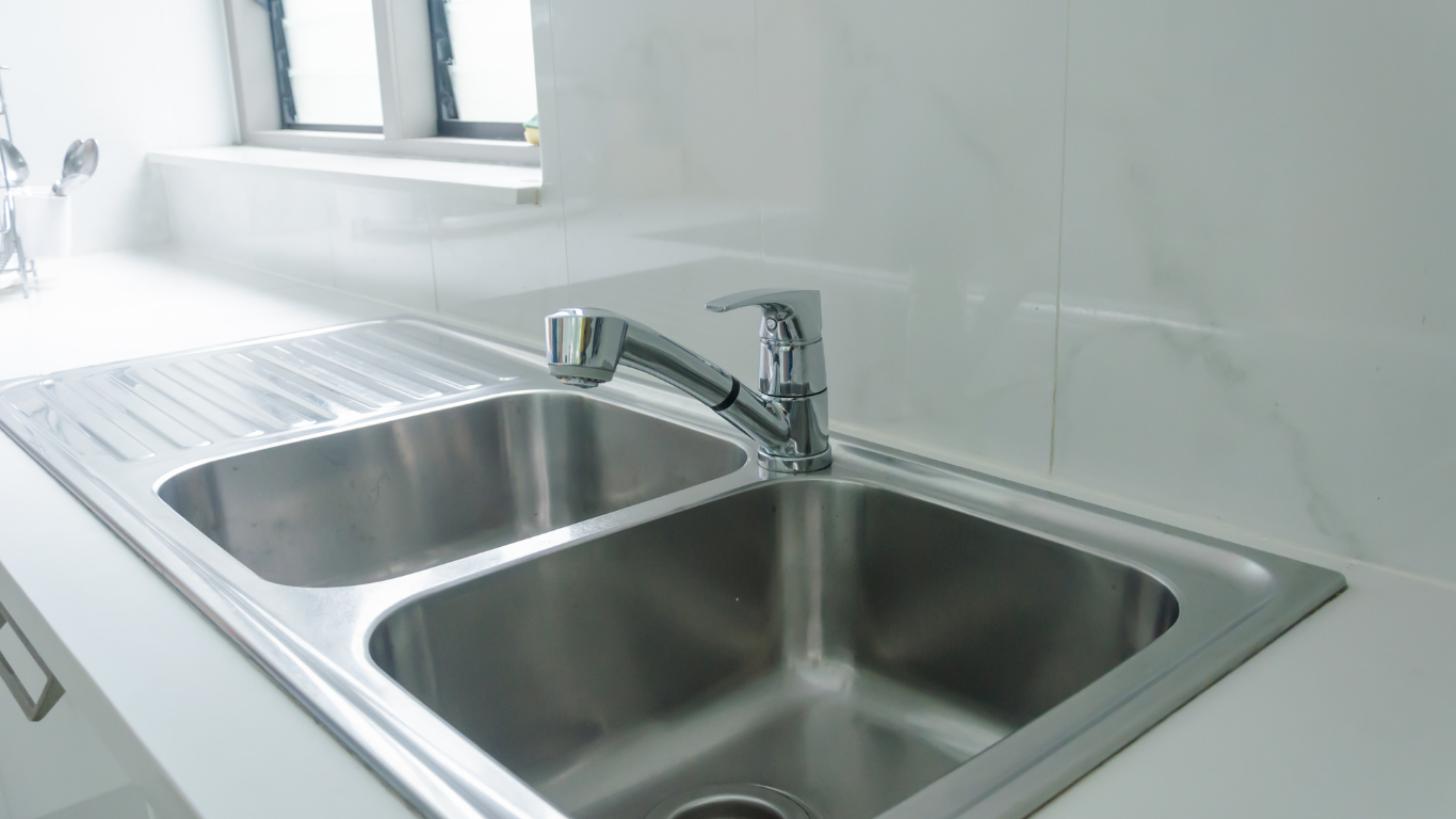 Stainless steel kitchen sink with faucet and white countertop.
