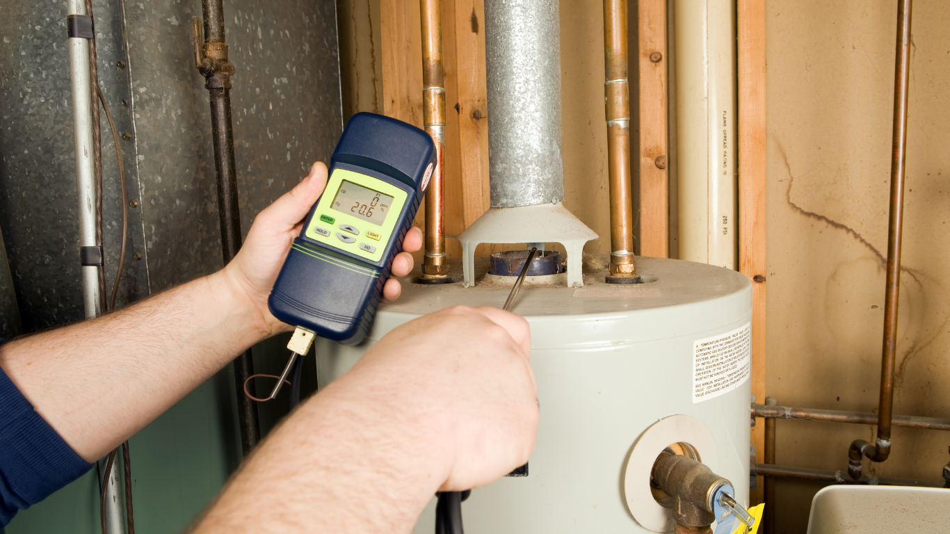 Person using a handheld thermometer to measure the temperature of a hot water heater in a utility room.