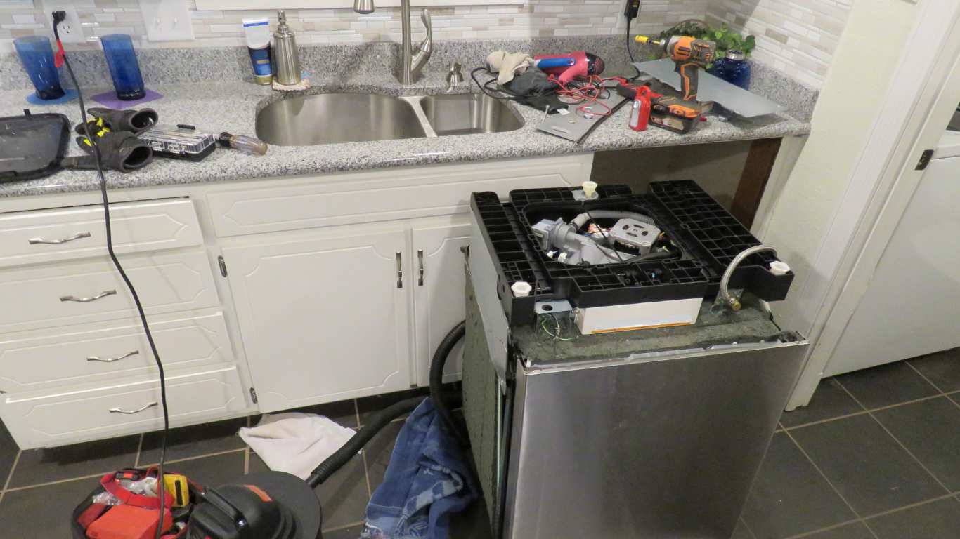 Dishwasher repair in a kitchen with tools, sink, and cabinets visible.