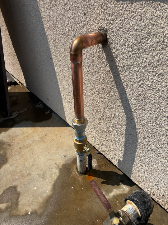 Undersink plumbing: grey drain pipes, flexible hose, garbage disposal, and wooden cabinet interior.