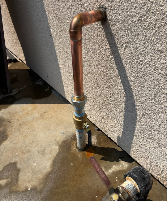 Copper pipes being soldered with a torch and silver solder at a T-fitting, indoors.