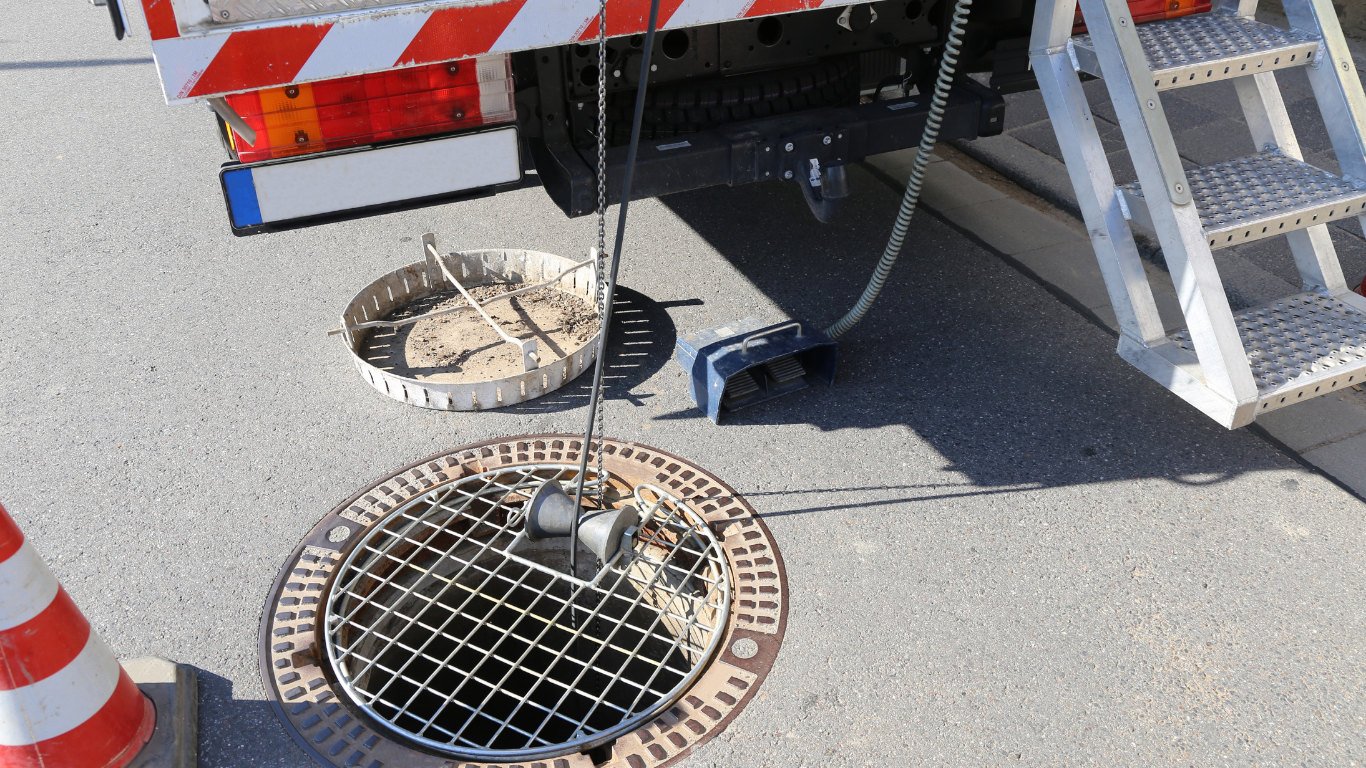 Person using a wrench on a leaky sink pipe; water is spraying.