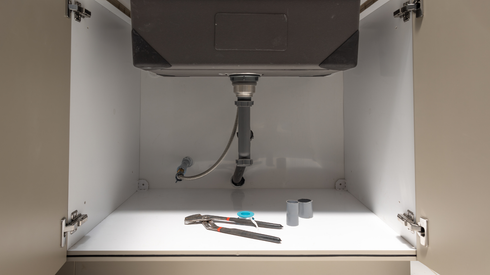 Underside of a bathroom sink showing plumbing. A corrugated drainpipe, and a curved pipe are visible.