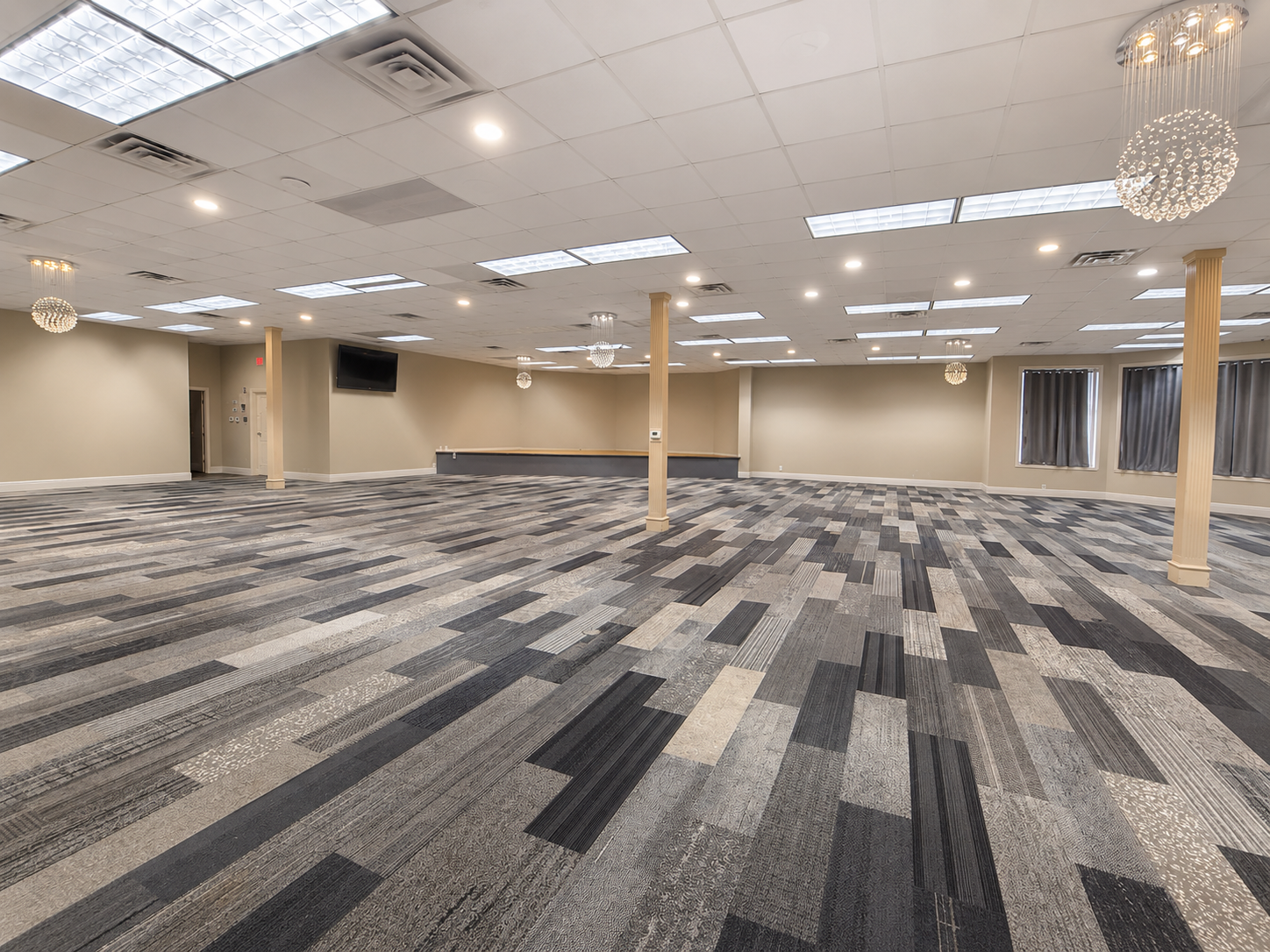 Empty conference room with gray patterned carpet, drop ceiling lights, and chandeliers.