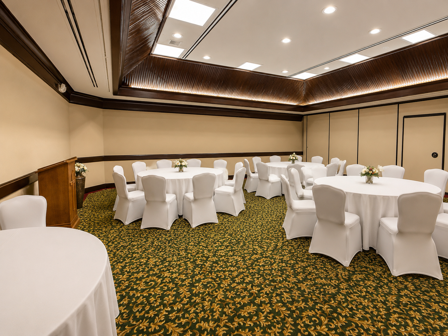 Banquet room with round tables draped in white linens and chairs on a patterned carpet