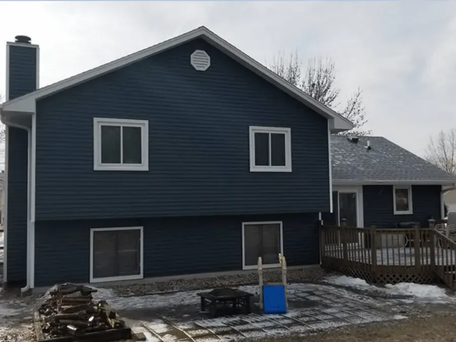 Back of a two-story blue house with white trim. A deck is attached to the house. Snowy ground.