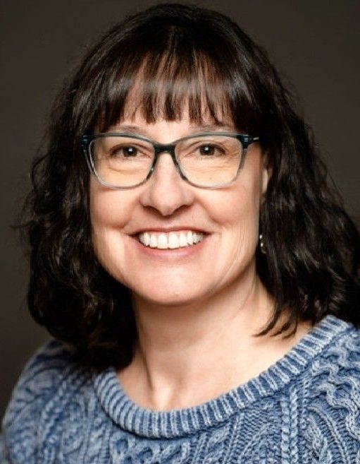 A woman wearing glasses and a floral shirt is smiling for the camera.