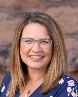 A woman wearing glasses and a floral shirt is smiling for the camera.