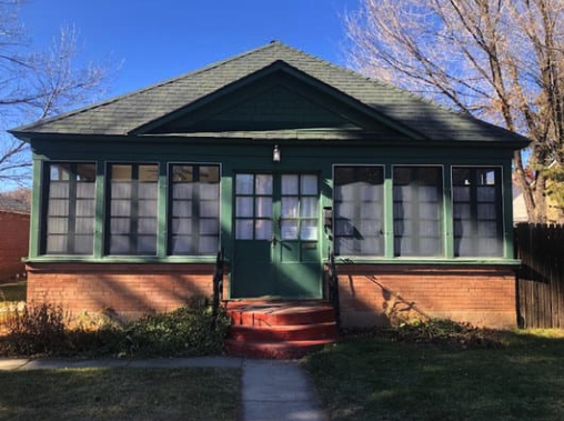 A small house with a green roof and a screened in porch.