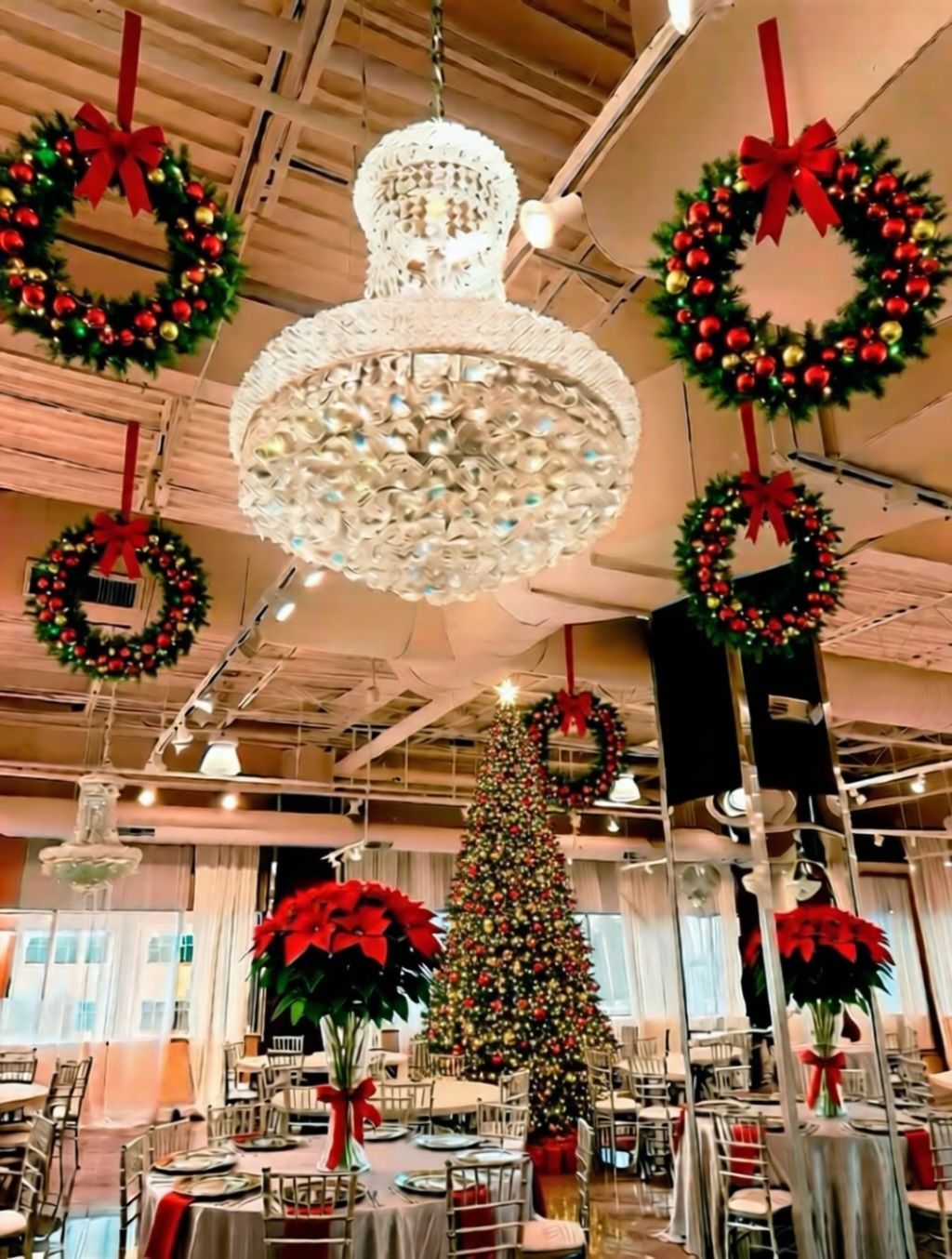 Christmas decorations in a venue: wreaths, chandelier, decorated tree, and tables set for dining.