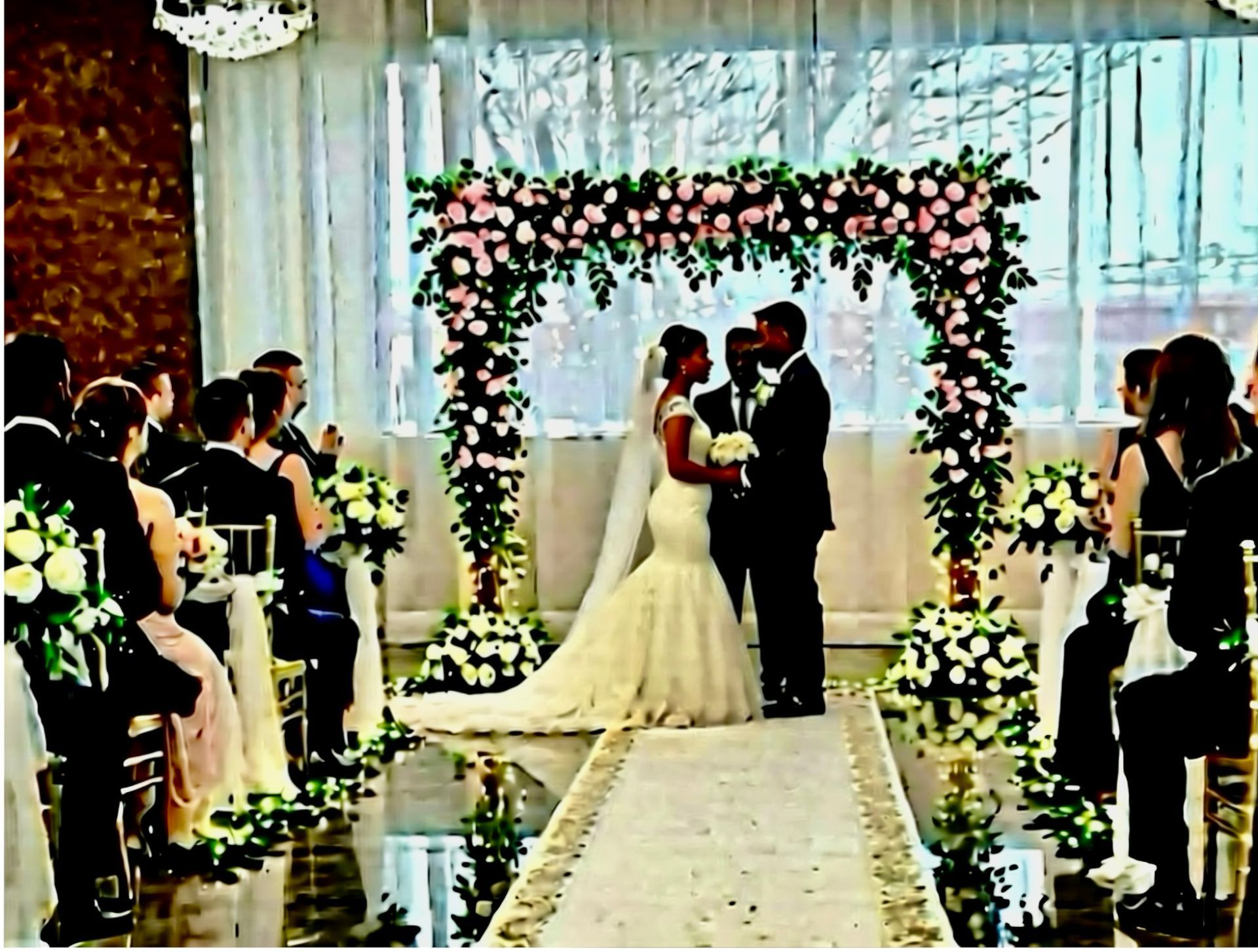 Wedding ceremony; couple under floral arch, guests seated, aisle runner.
