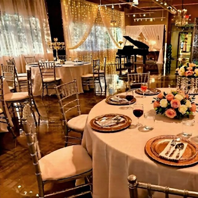 Elegant event space with round tables set for dining, a piano, and gold lighting.