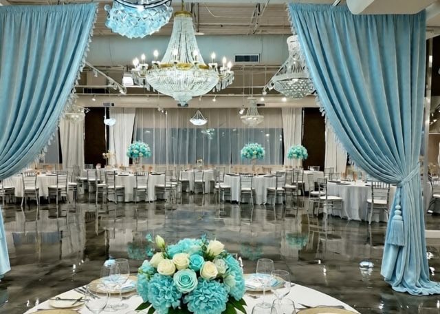 Elegant event space with round tables, teal floral centerpieces, chandeliers, and teal curtains.