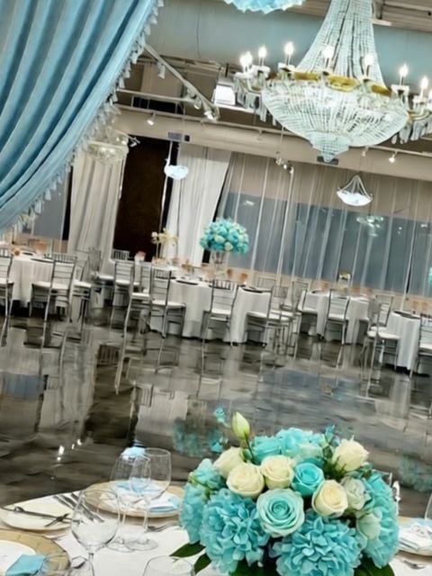 Elegant event space with tables, chairs, and centerpieces; blue and white color scheme.