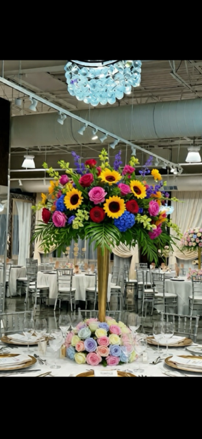 Wedding table centerpiece with sunflowers, roses, and hydrangea; venue with tables and chairs.