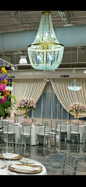 A brightly lit event hall with tables set for a celebration. A large chandelier hangs overhead.