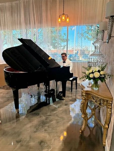 Pianist playing a black grand piano in a room with a gold console table and floral arrangement.