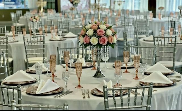 Elegant wedding reception with white tablecloths, floral centerpieces, and silver chairs.