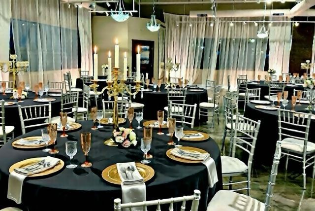Elegant event space with round tables, black tablecloths, gold chargers, silver chairs, and candles.