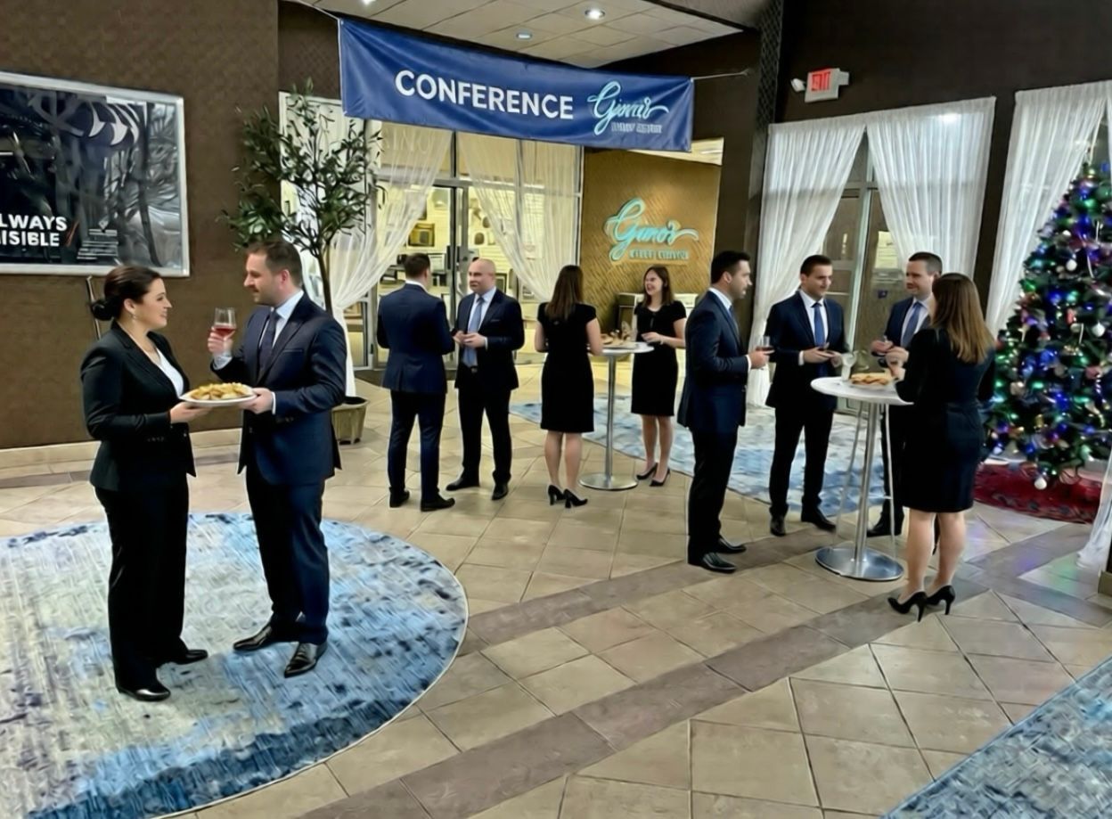 People networking at a conference, some with drinks and snacks.  Indoor setting with a Christmas tree.