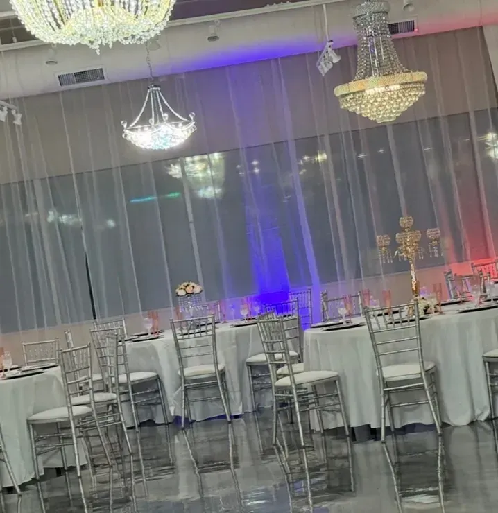Elegant banquet hall with chandeliers, tables set with white linens and silver chairs.