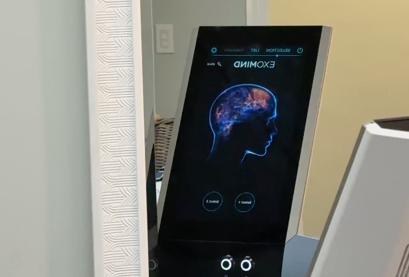 A close-up of a digital kiosk screen displaying a glowing, stylized brain graphic with the text 