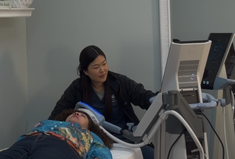 A technician operates a medical brain stimulation device on a person lying on an examination table.