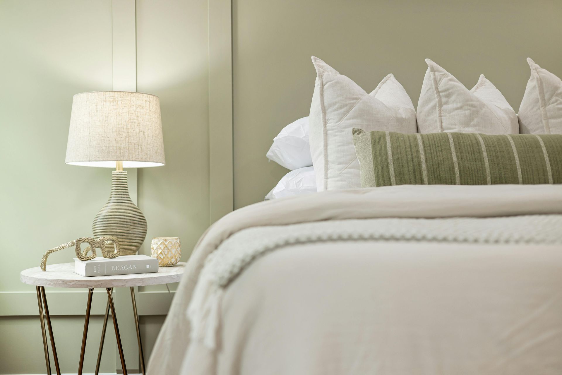 Bedroom with bed, lamp, side table, and green accent pillows.