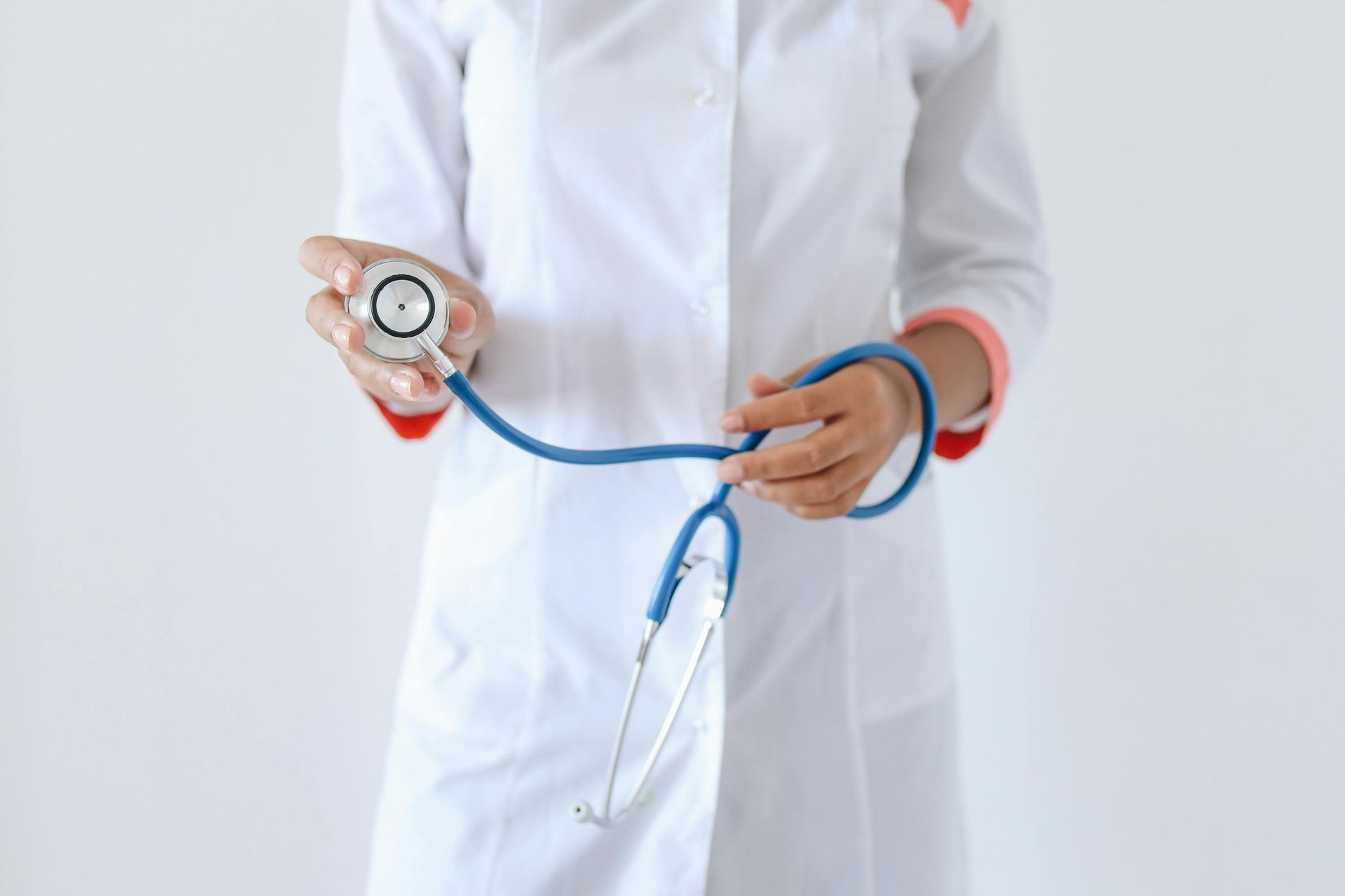 Doctor holding stethoscope. White coat with red trim, blue stethoscope.