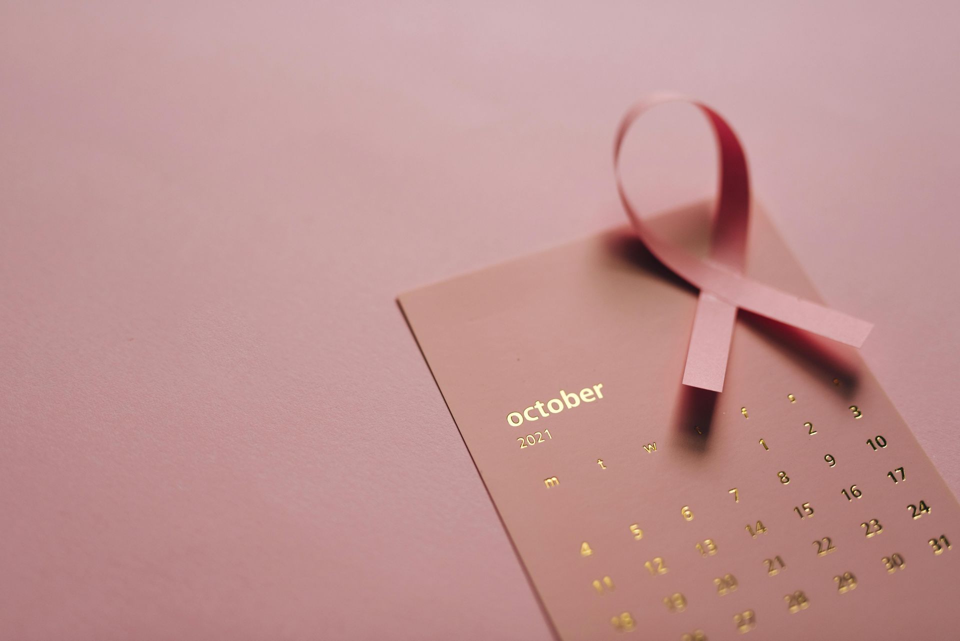 Pink ribbon on a pink calendar, symbolizing October and breast cancer awareness.