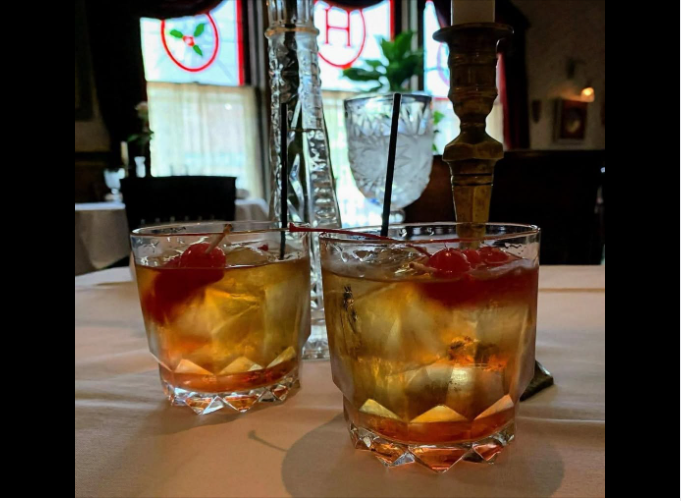 Two glasses of whiskey with cherries in them on a table