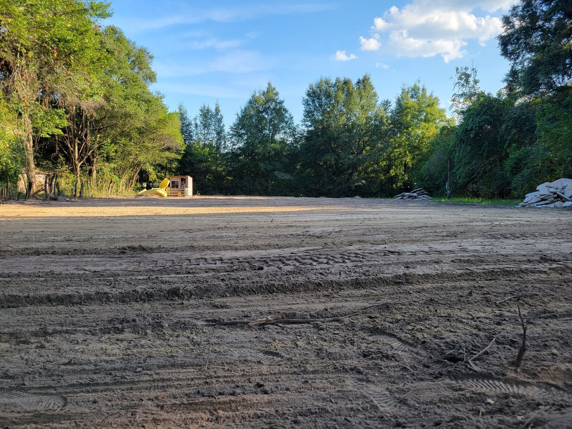 A dirt field with trees in the background and a blue sky.