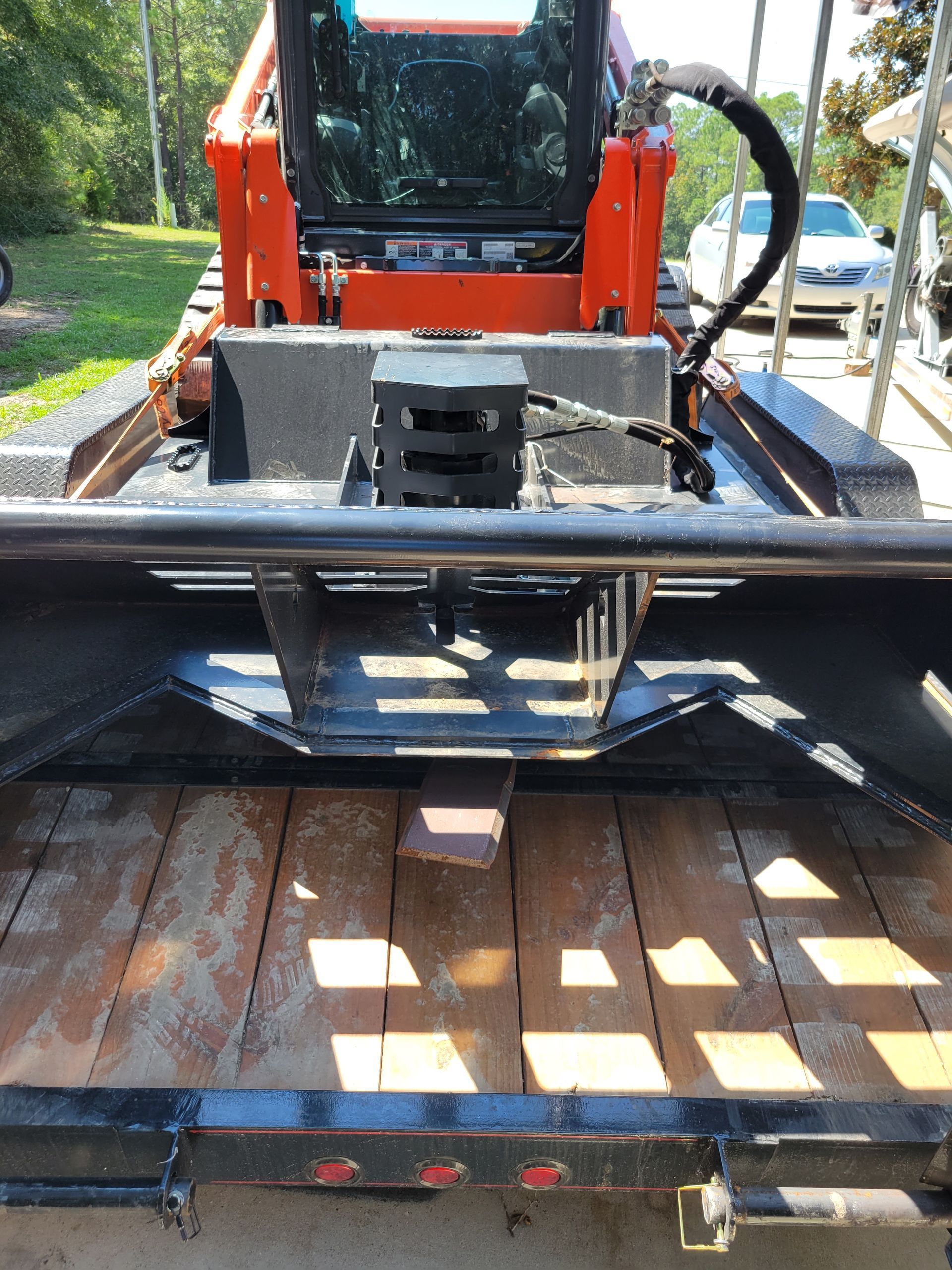 A small orange tractor is parked on a wooden trailer.