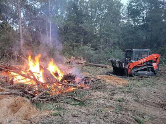 A bulldozer is sitting next to a fire in the woods.
