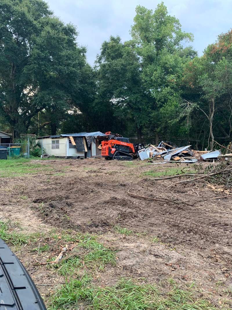 A tractor is sitting in the middle of a dirt field next to a house.